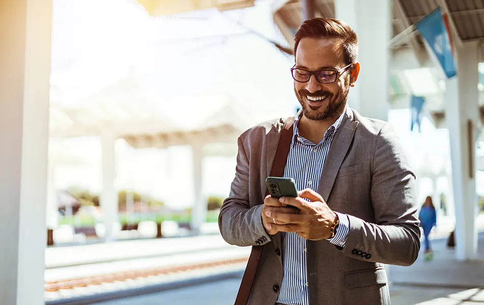 Man står utomhus och använder mobiltelefon vid tågstation.