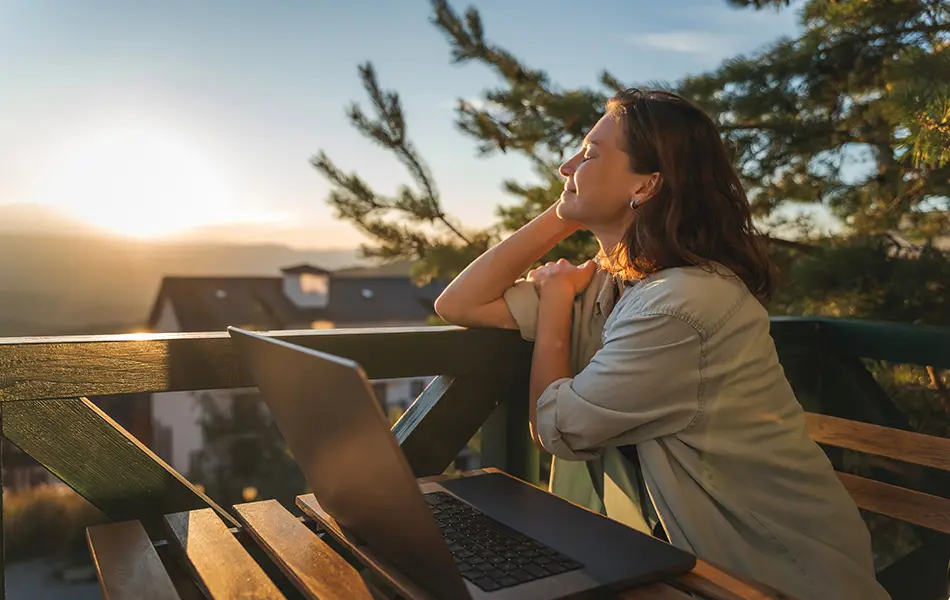 Kvinna med laptop på balkong i solnedgång.