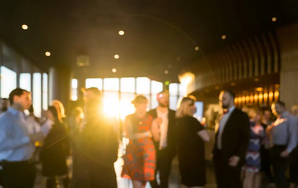 Grupp människor minglar i en lokal med solljus i bakgrunden.