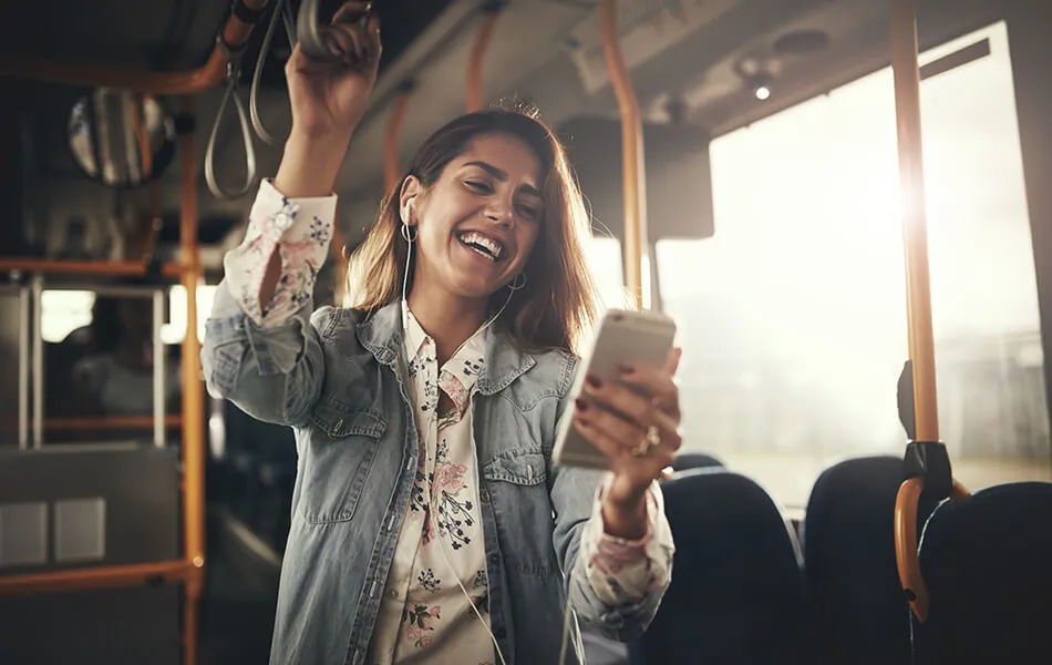 Glad tjej som står på bussen och tittar på mobilen