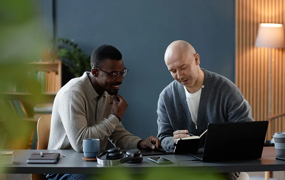 Två personer sitter vid ett bord och arbetar tillsammans med laptop och anteckningar.