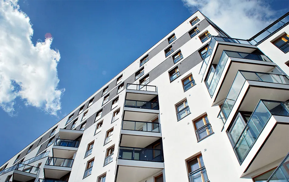 Modern lägenhetsbyggnad med glasbalkonger mot en blå himmel.