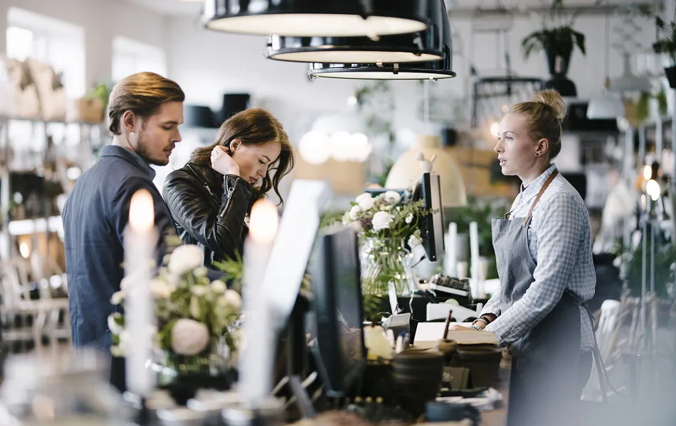Två kunder står vid kassan och pratar med en florist i en blomsterbutik.